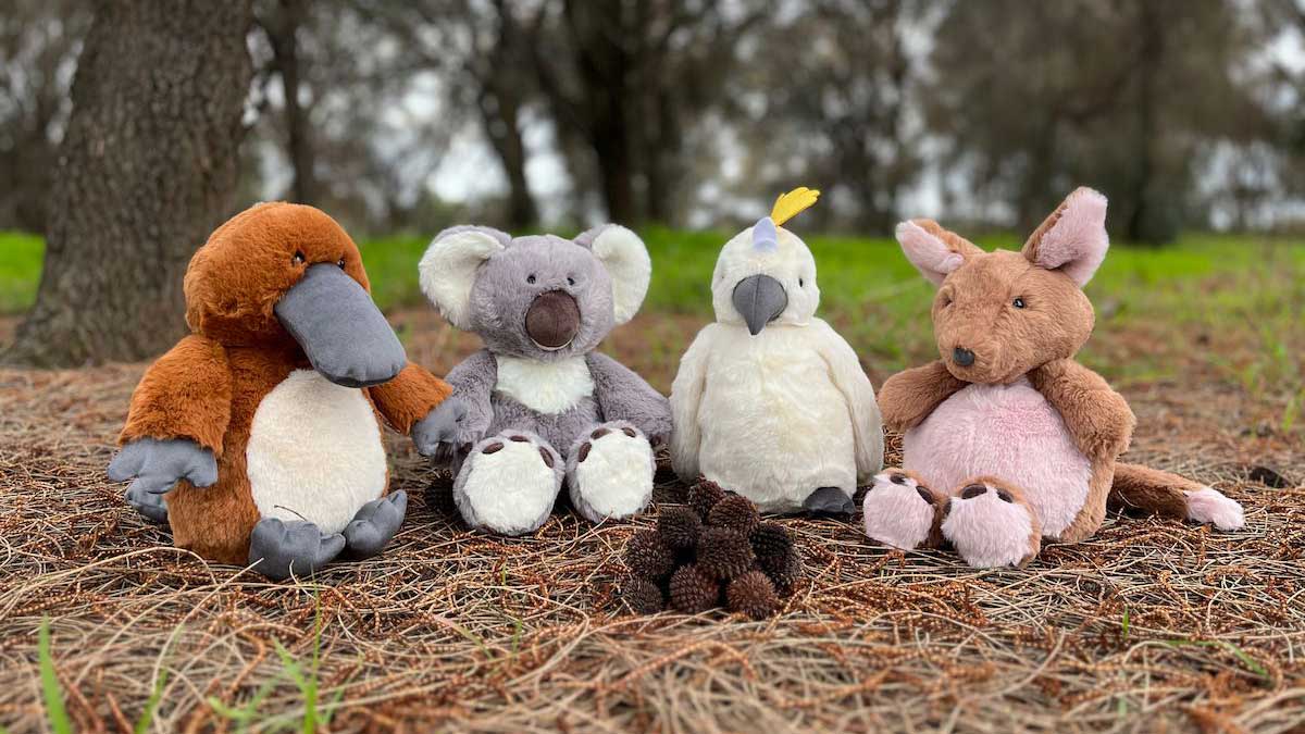 Platypus, koala, cockatoo and kangaroo plush toys sitting together in bushland